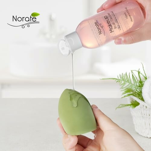 Hand pouring makeup remover onto a green sponge with Norate branding.